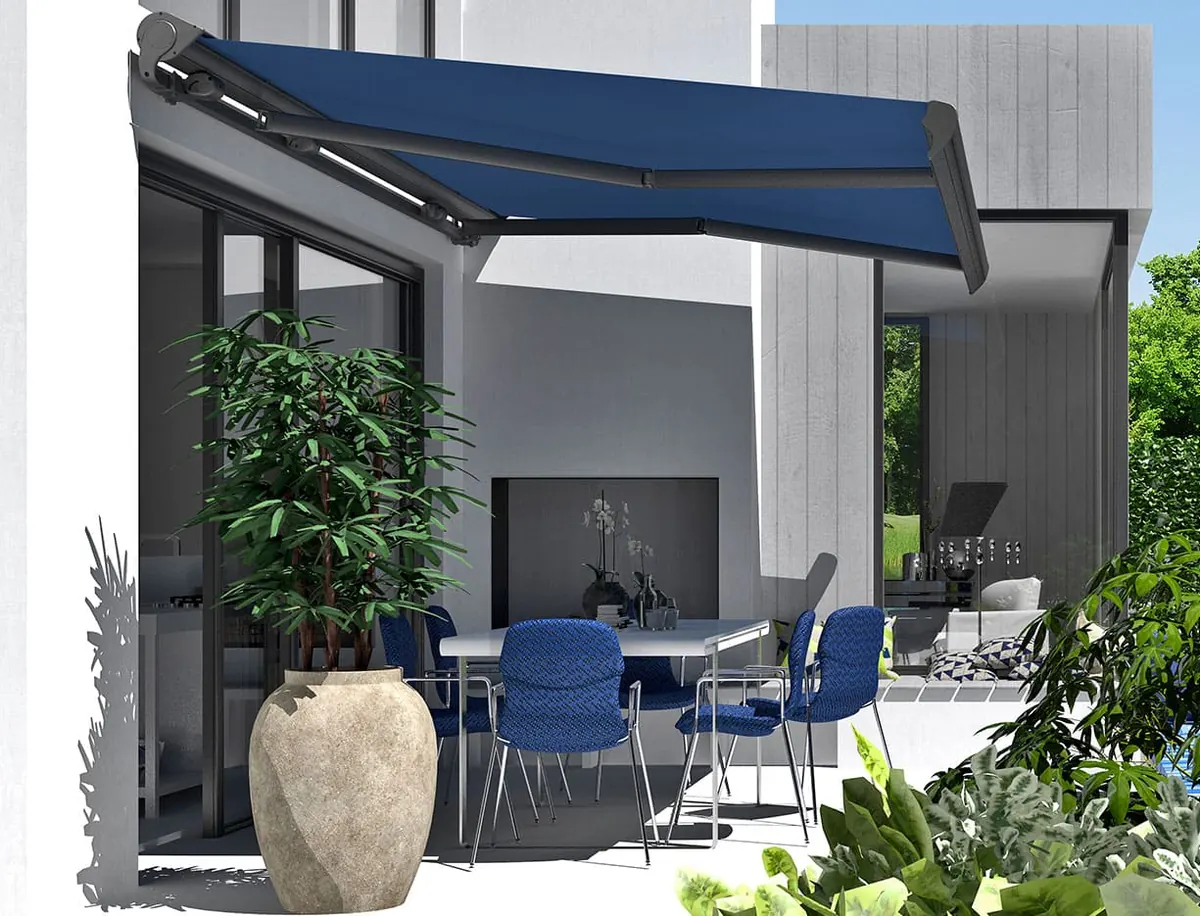 Blue folding-arm awning extended over a patio dining table and chairs next to a grey facade