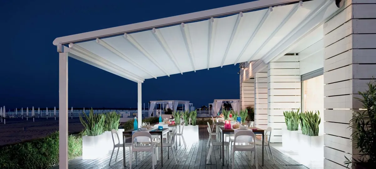 White canopy extended at night over outdoor dining tables on a lit terrace