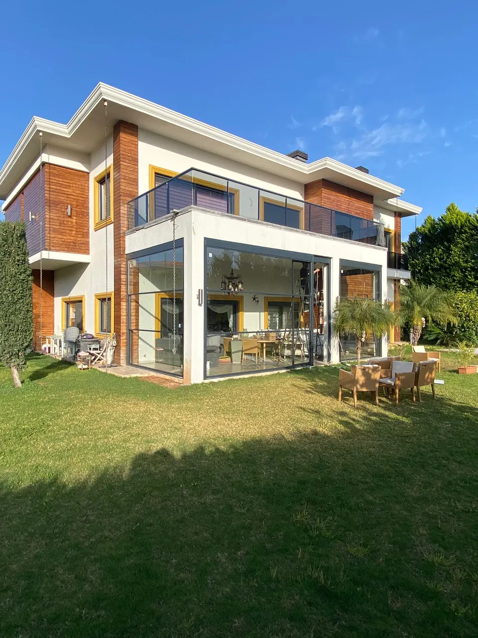 Villa terrace enclosed with dark-framed glass walls beneath an upper balcony