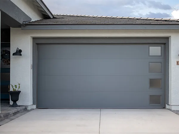 Grey sectional garage door with small windows on a white house front