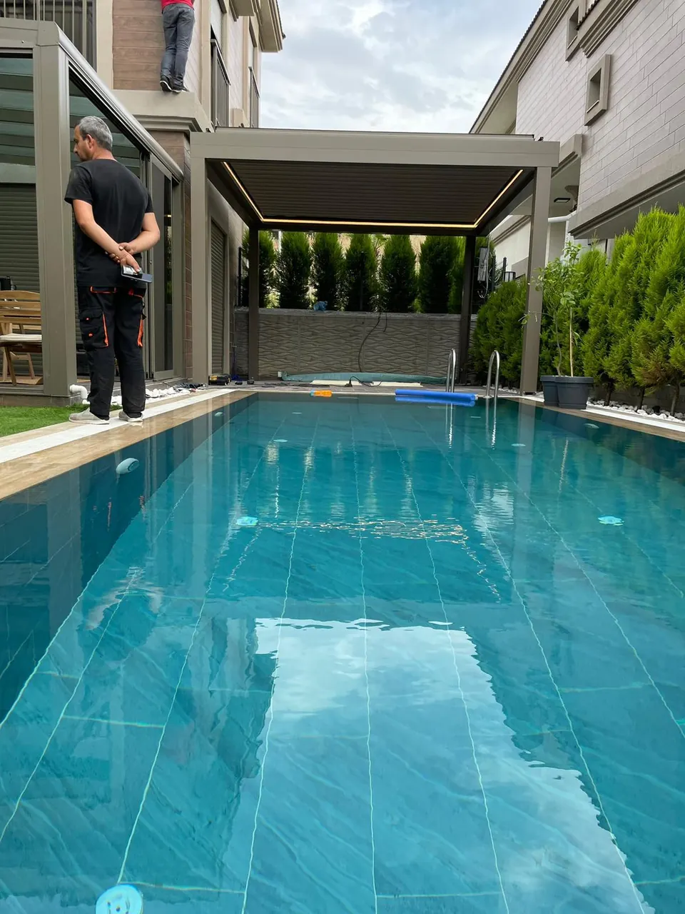 Piston bioclimatic pergola beside a pool, with a technician at the installation