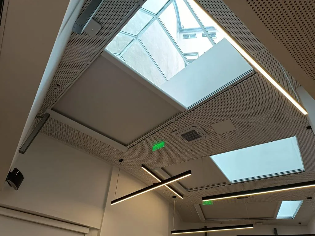 Office ceiling with several skylights each fitted with a zip screen and linear lighting