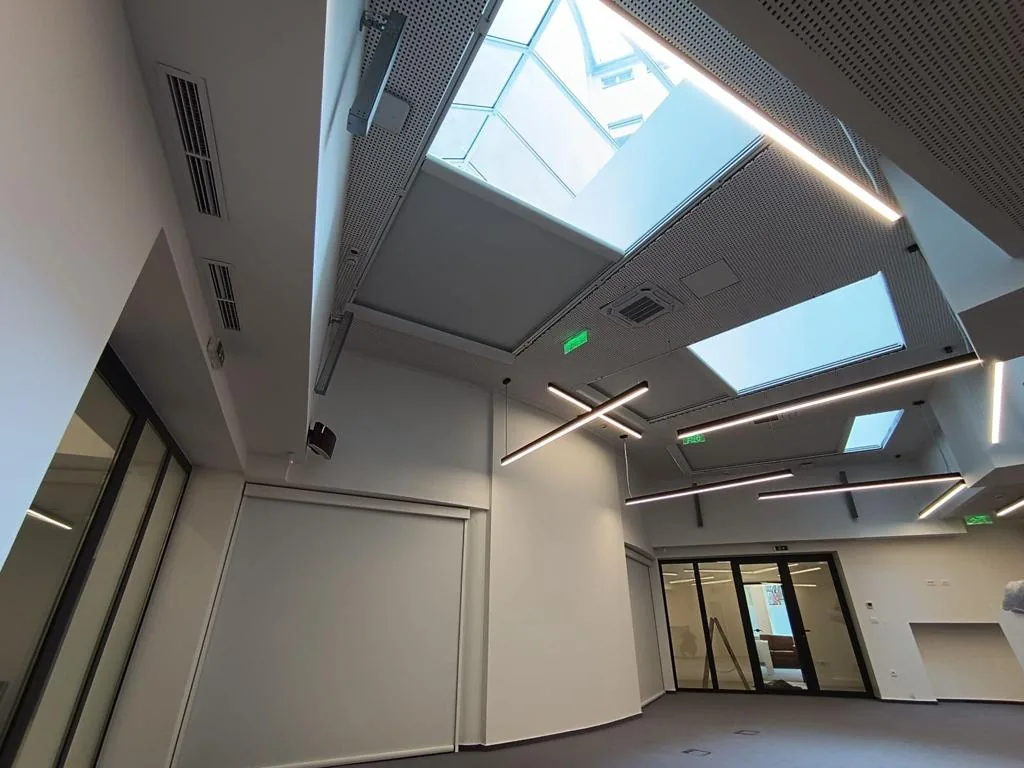Interior space with skylights overhead and a lowered screen over the glazed doors