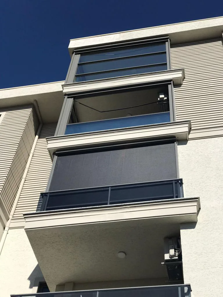 Dark zip screens lowered over the balconies of a multi-storey residential building under a blue sky