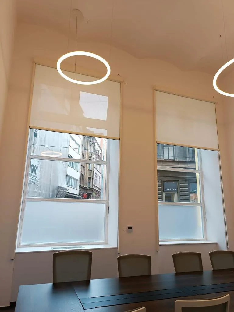 Light roller screens covering tall windows in a meeting room with a long table