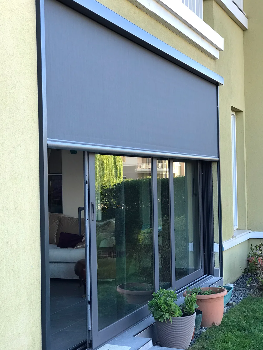 Tall grey zip screen above a glazed sliding door on the ground floor of a yellow-walled building