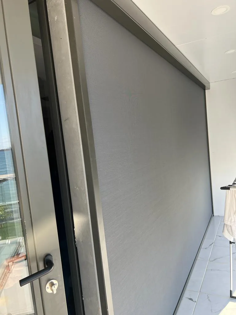 Close view of a grey zip screen edge beside a door handle and glazed door frame