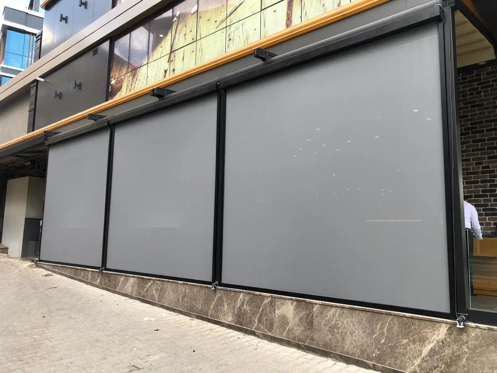 Row of three grey zip screens along a street-front glazed façade under a timber-clad canopy