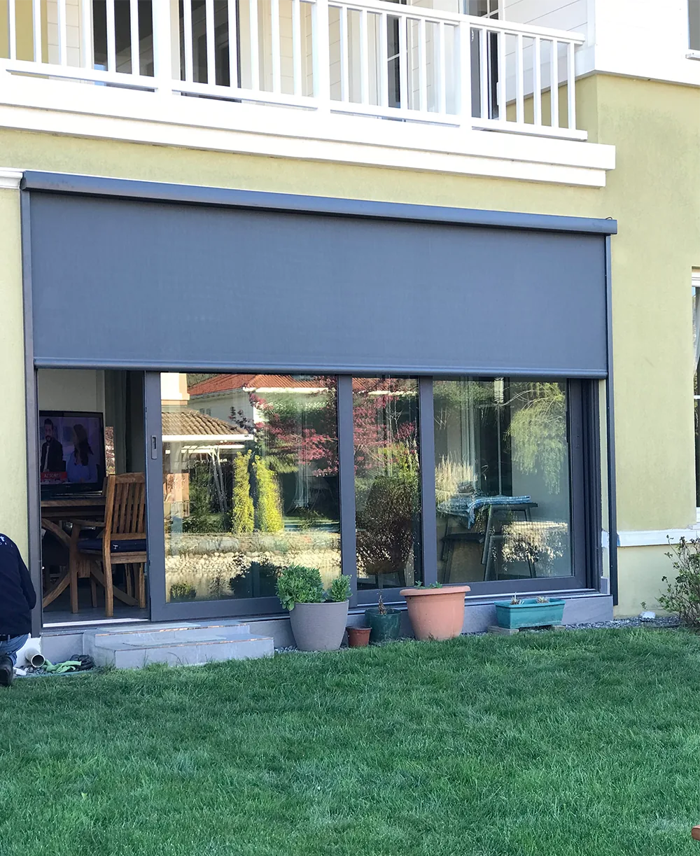Grey zip screen lowered over the glass doors of a ground-floor unit with a lawn in front