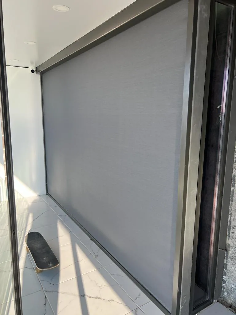 Single large grey zip screen lowered inside a dark frame beside a glazed door