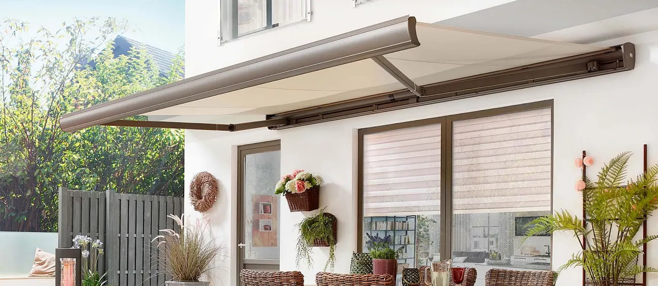 Cream cassette awning with brown frame extended over a patio with shuttered windows