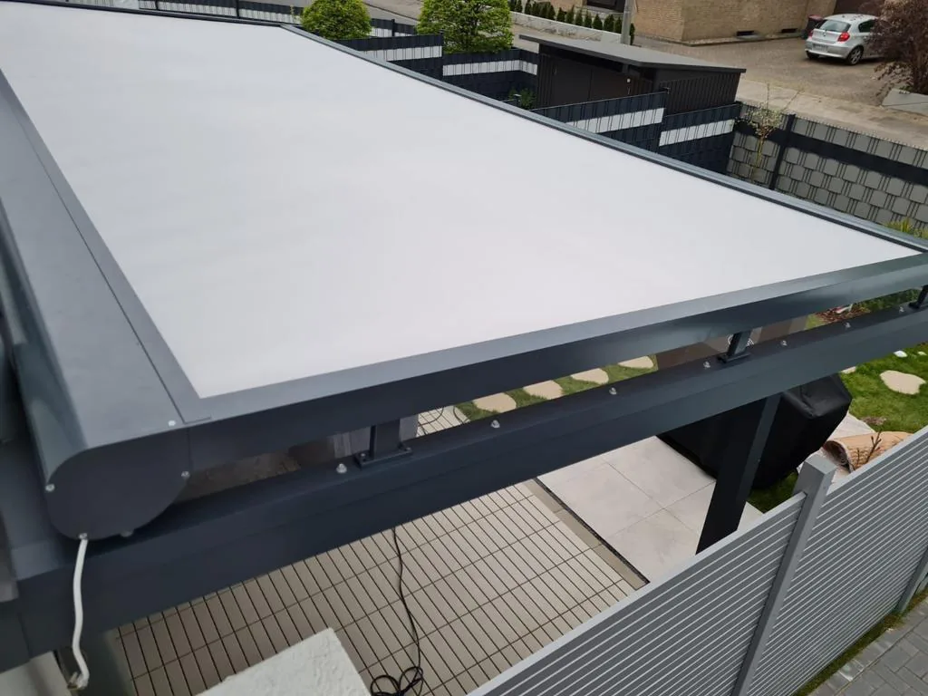Close view of a grey zip screen lying over a dark-framed glass roof, with a garden path beside it