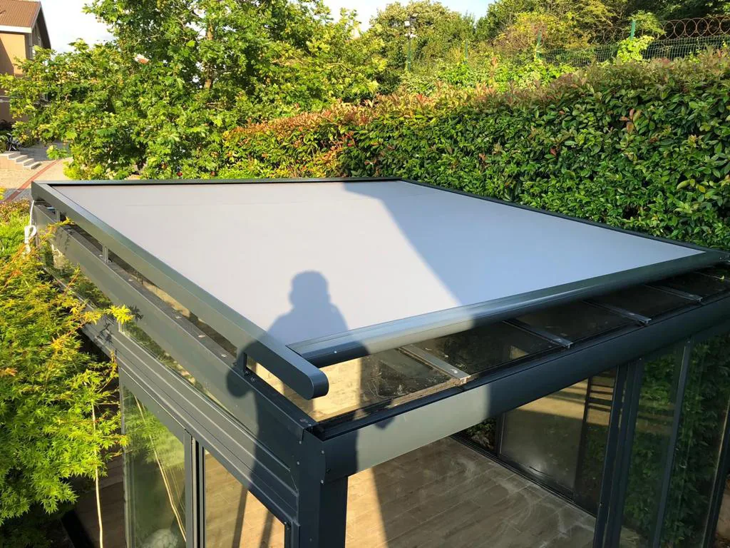 Grey roof screen over a glazed winter garden, photographed from the garden side with hedges around