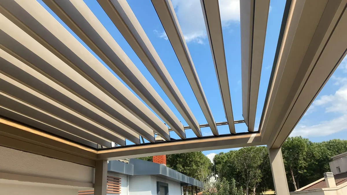 Underside of scissor bioclimatic louvres opened against blue sky with warm LED line along the beam