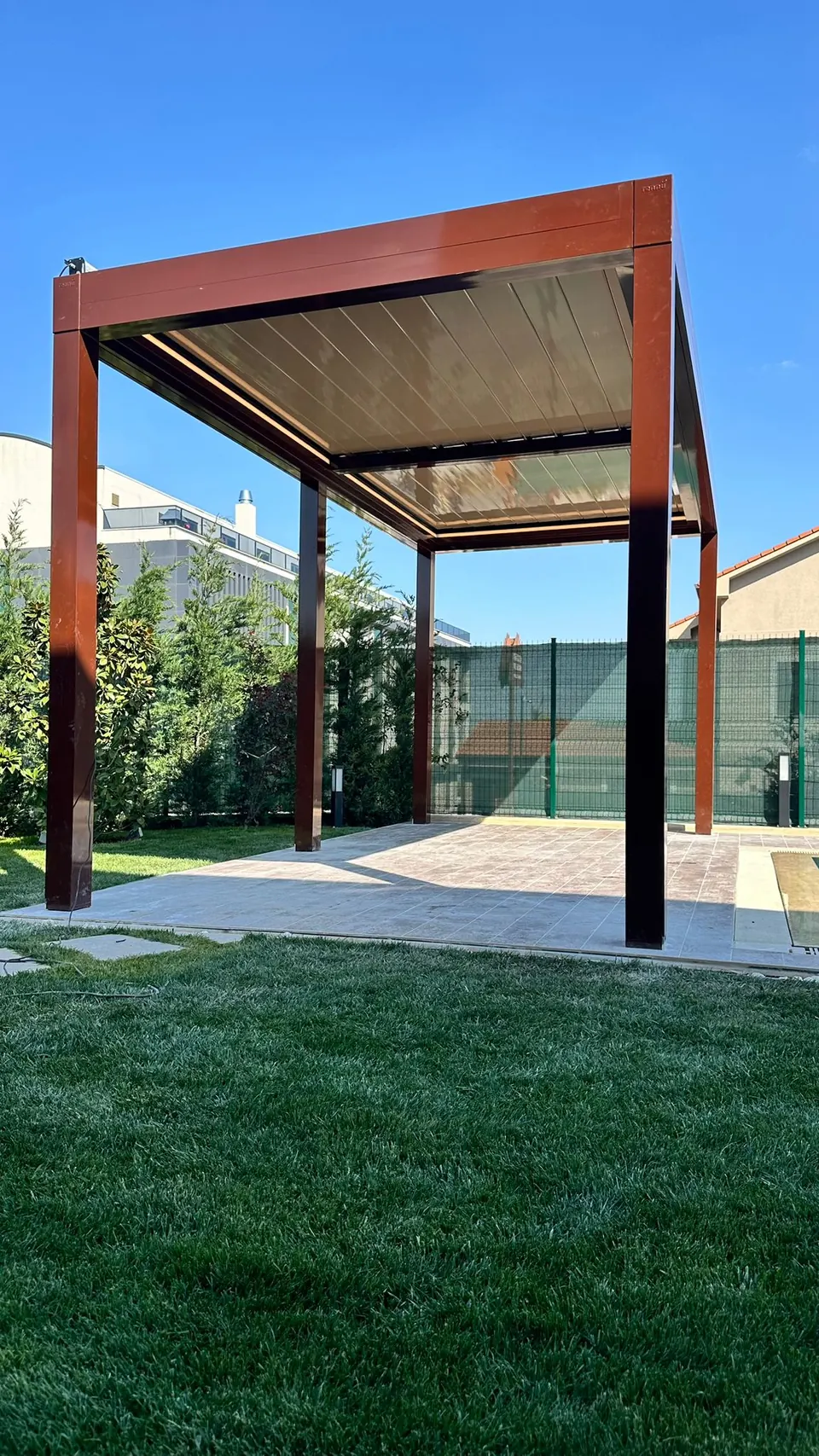 Scissor bioclimatic pergola in a garden with dark red posts and roof panels closed