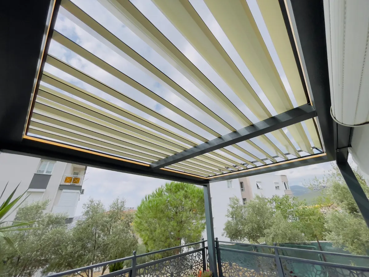 Cream louvres of a scissor bioclimatic roof tilted open above a balcony terrace, seen from below