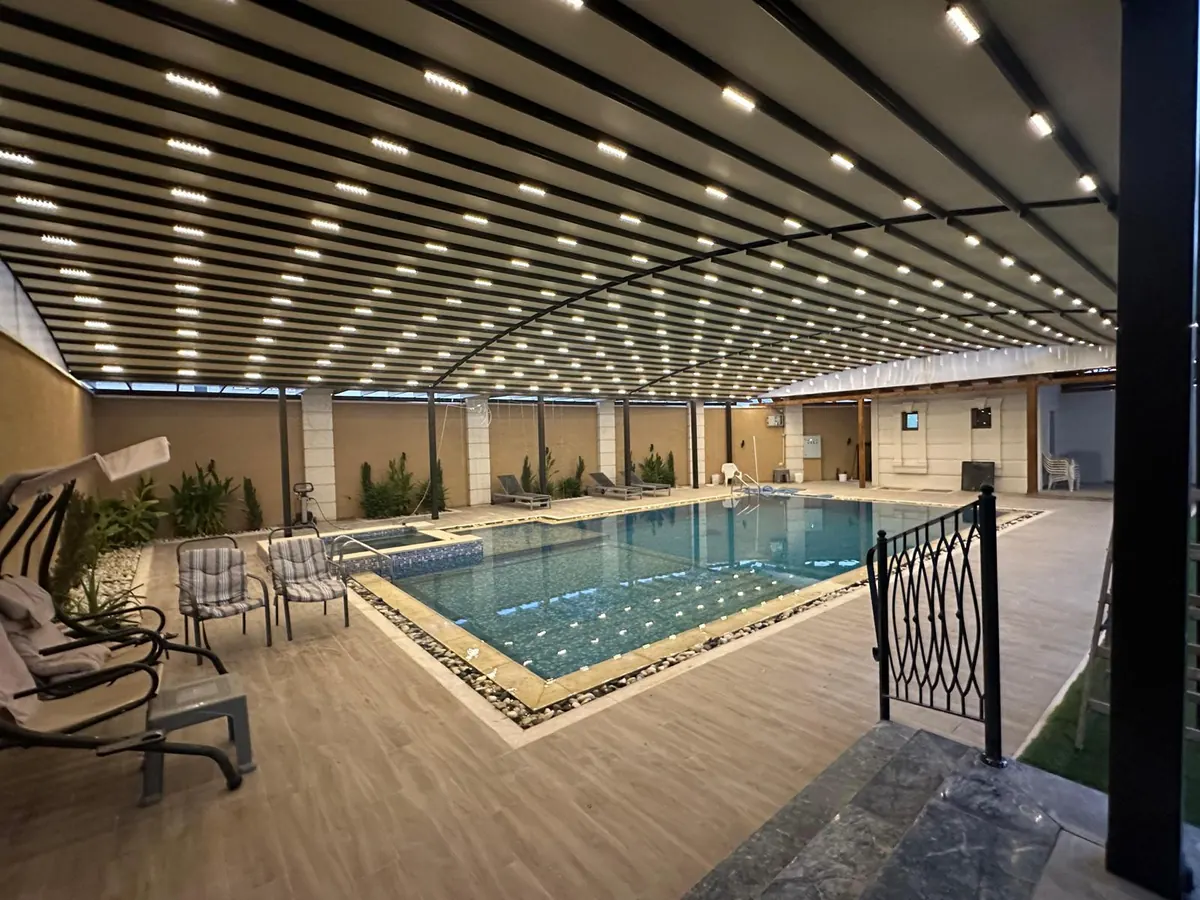 Retractable shade structure with recessed lights above an indoor pool and loungers