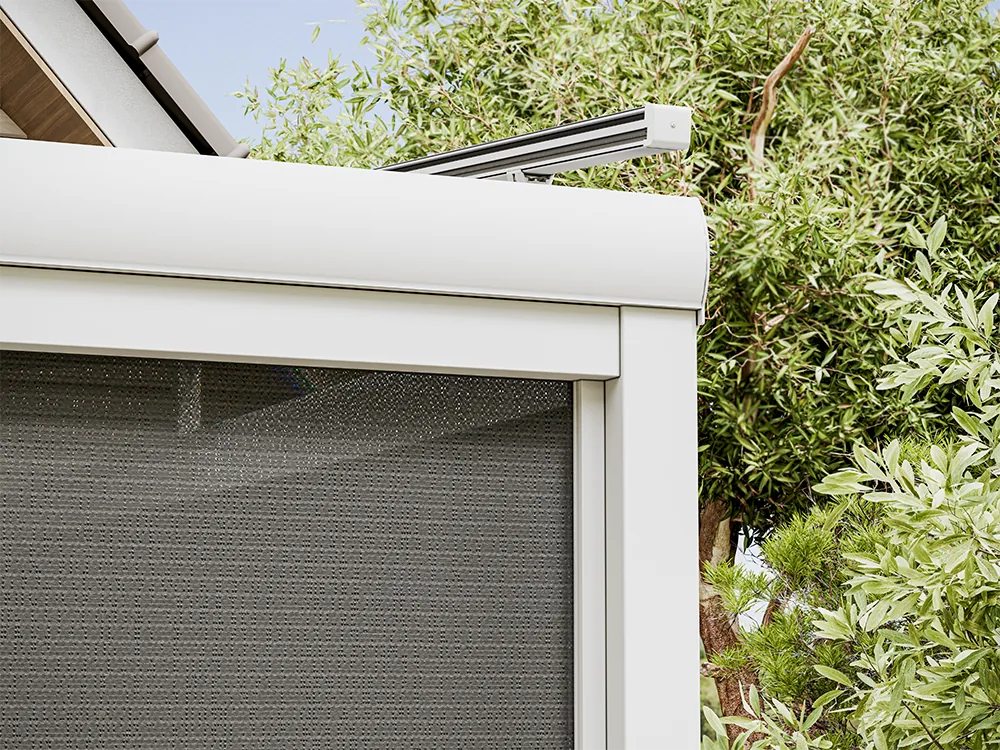 Close-up of a white headbox above grey mesh zip screen fabric beside a garden tree