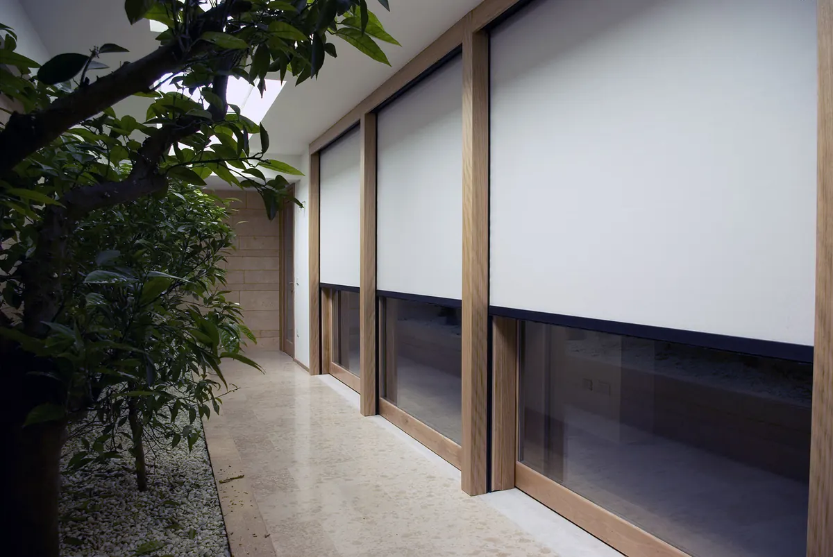 Row of vertical zip screens in timber frames shading a glazed facade corridor