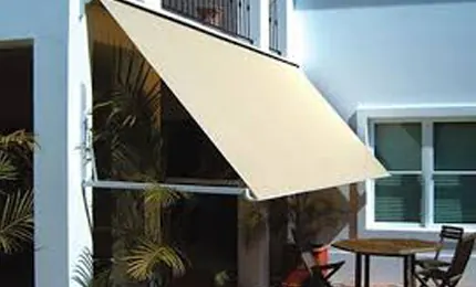 Beige window awning projecting over a first-floor window with a balcony railing above